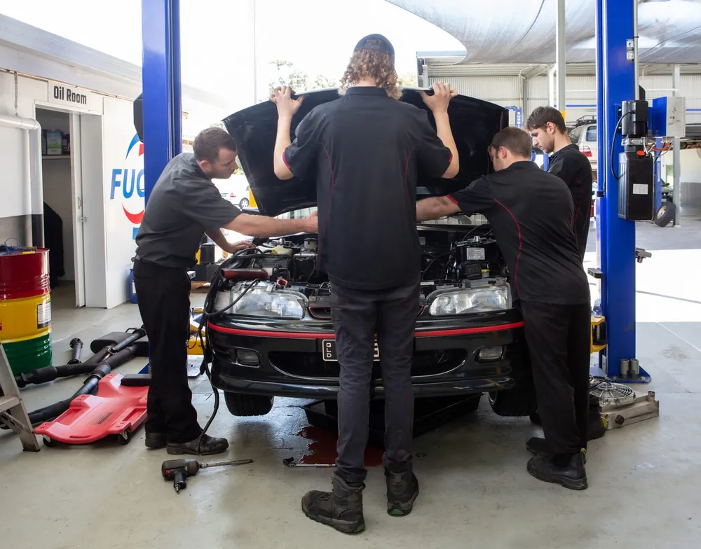 Four mechanics around the open engine bay of a car