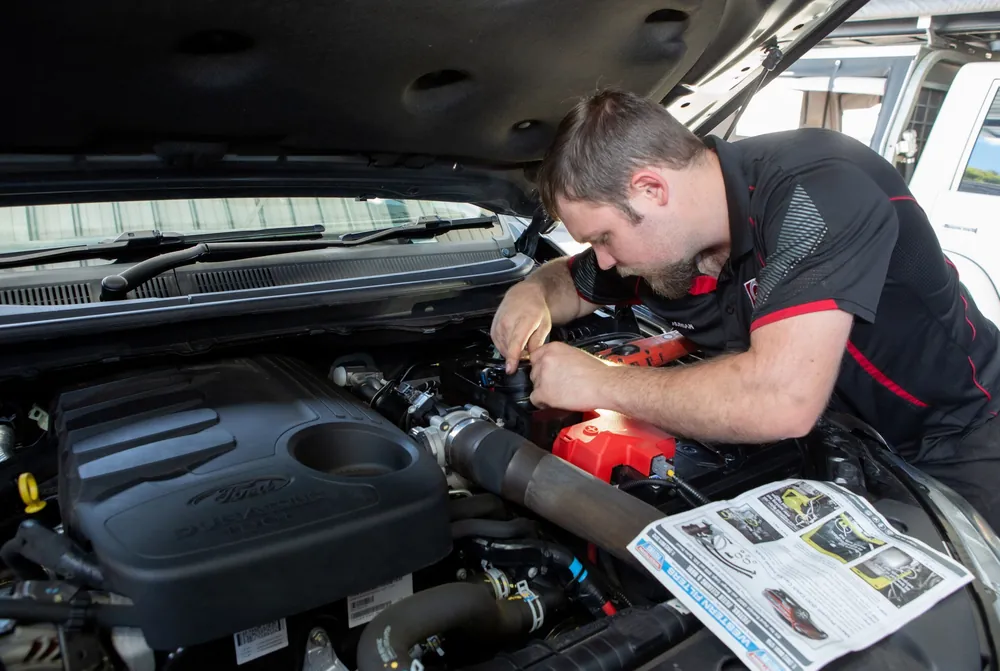 A mechanic working in an engine bay with the service manual open